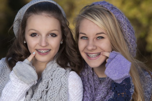 Two teenage girls smiling as they point to their braces