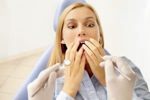 A young woman in a dentist chair looks afraid