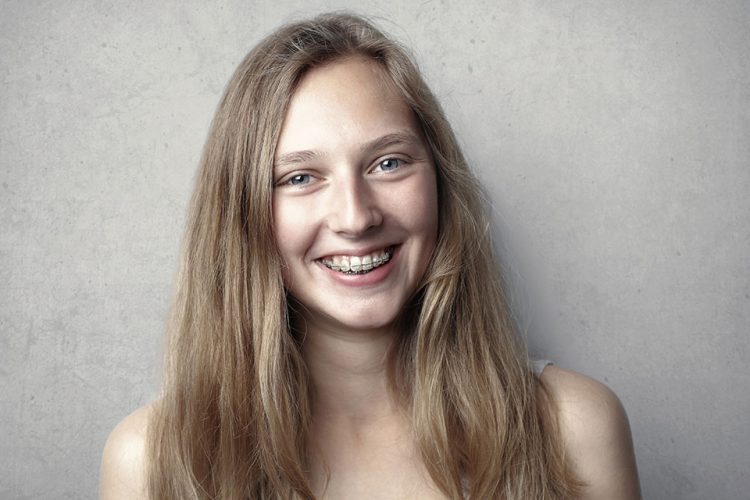 Young female presenting person with long blond hair smiling with braces